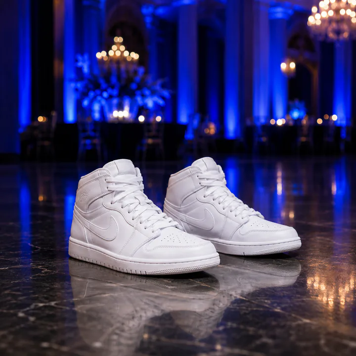 Pair of clean white sneakers on a reflective floor in a blue-lit event hall.