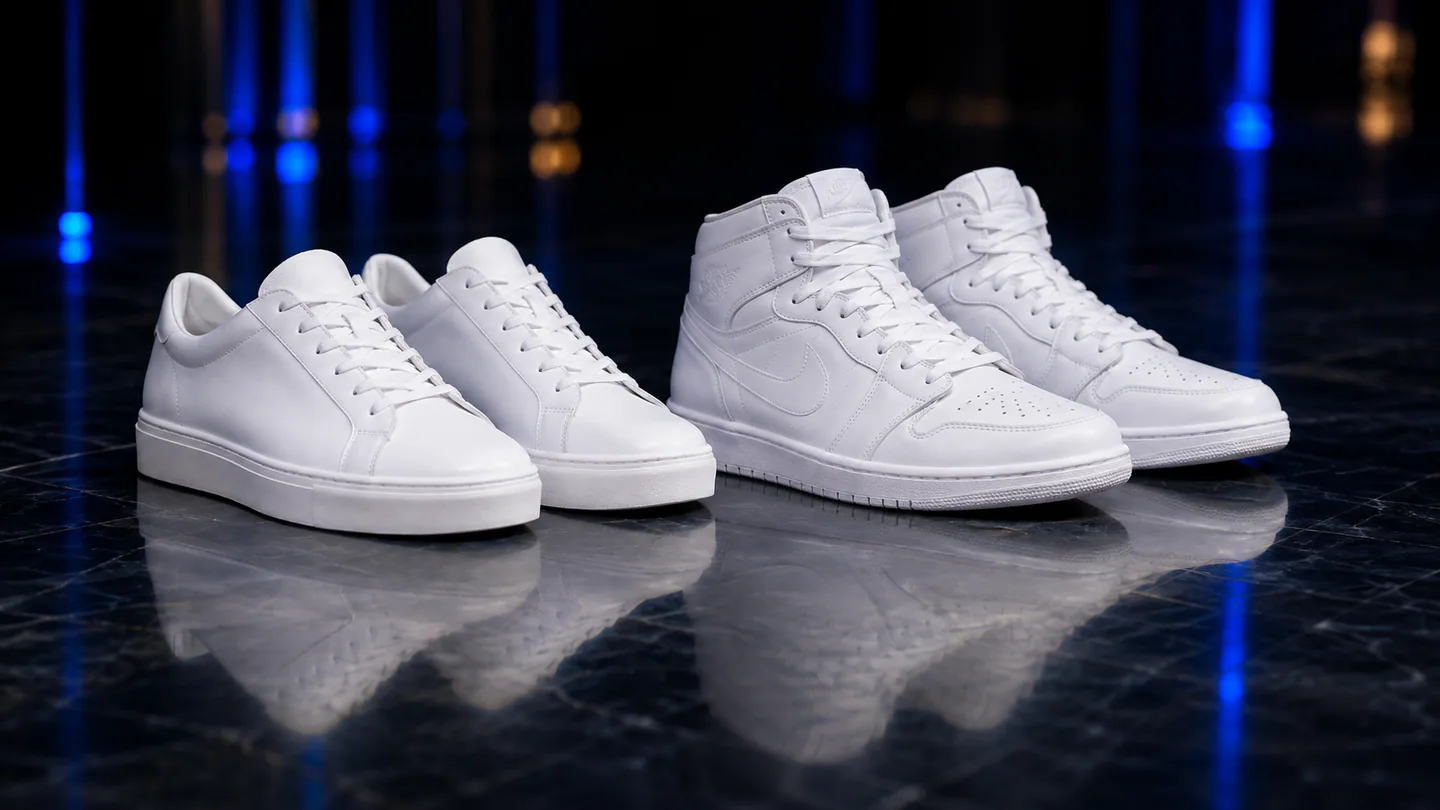 Four clean white sneakers on a reflective dark floor with royal-blue lighting.